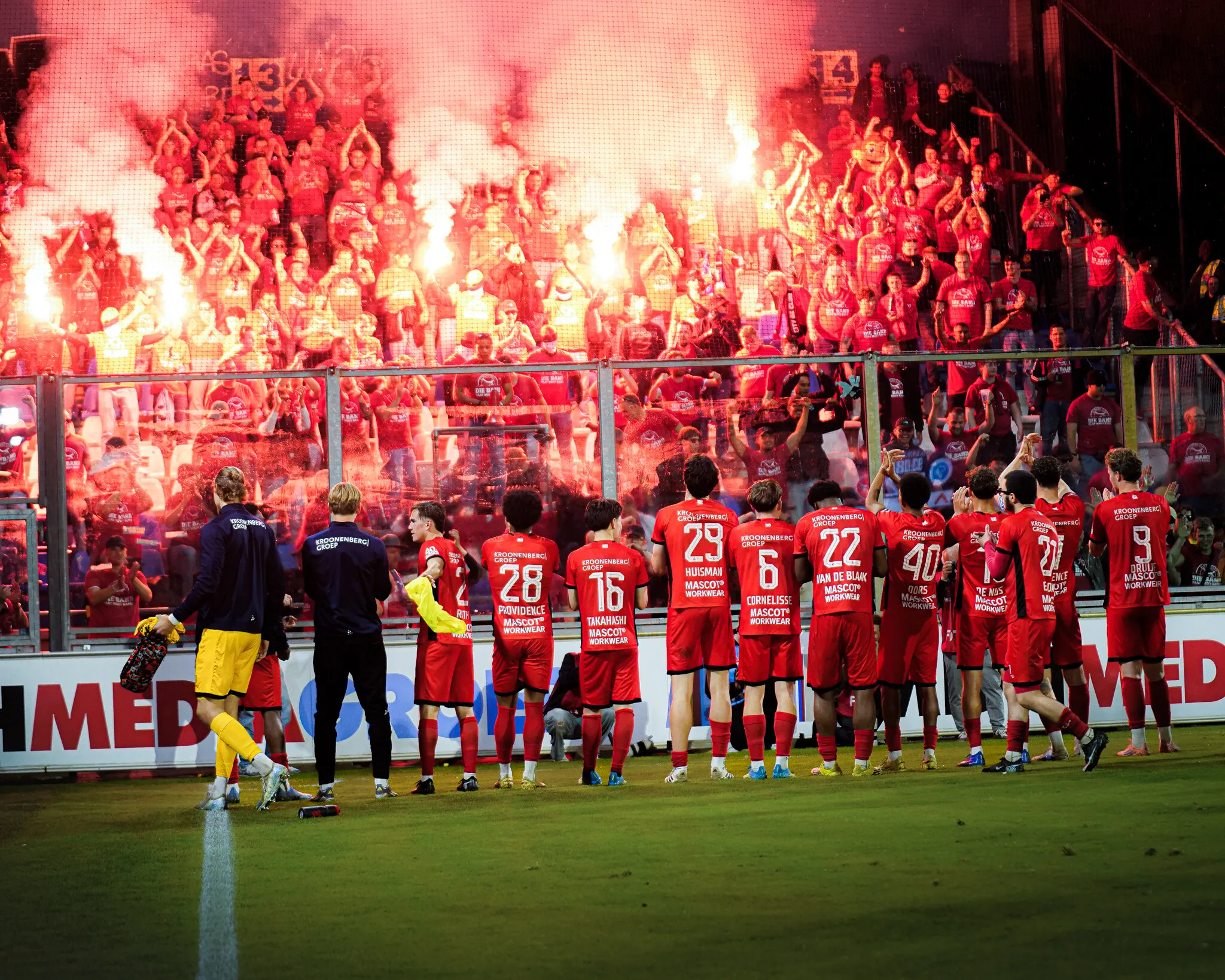 Spelers bedanken het supportersvak terwijl er rode fakkels branden op de tribune