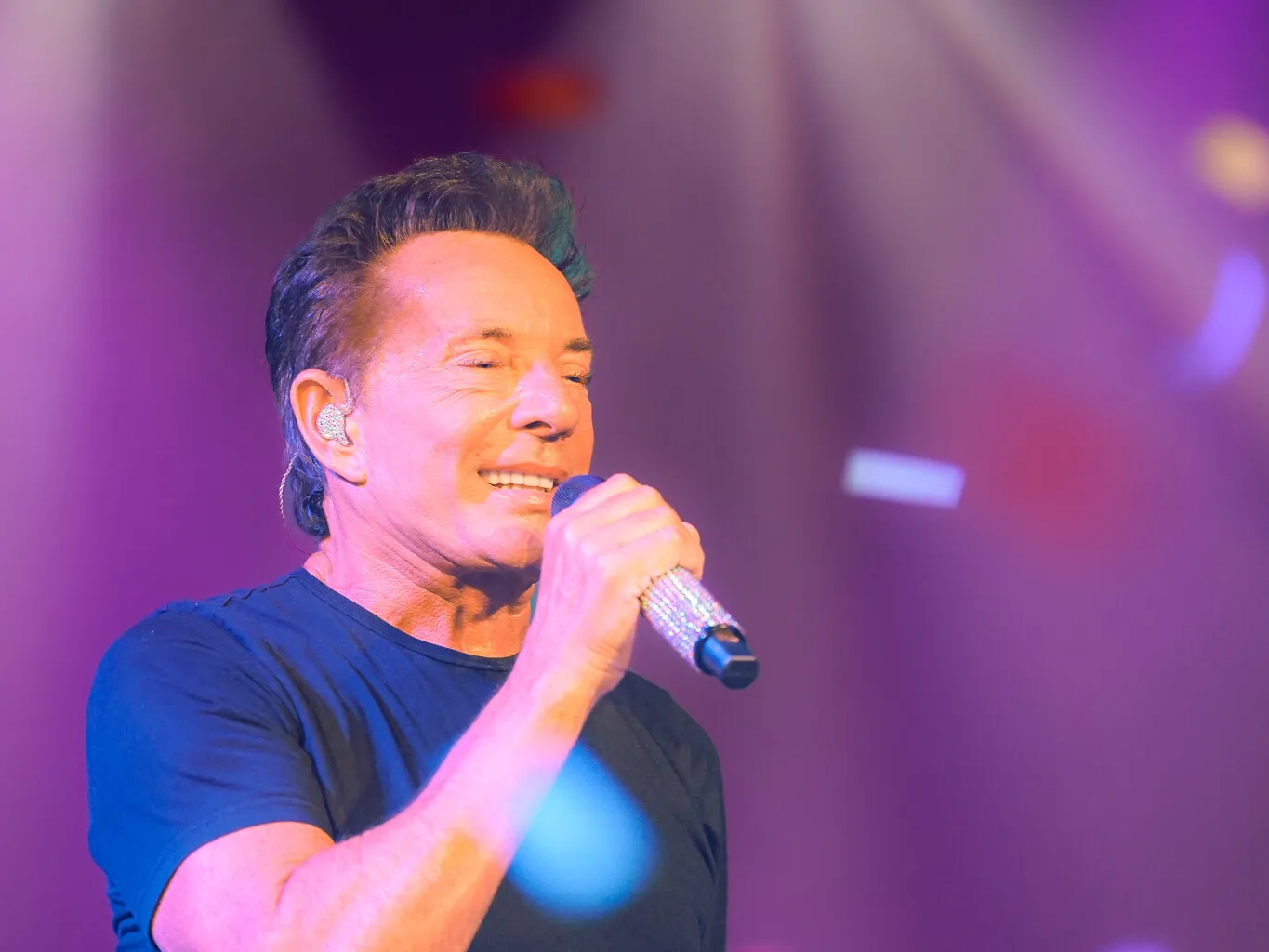 Artiest zingt in de microfoon onder paars podiumlicht met confetti in de lucht