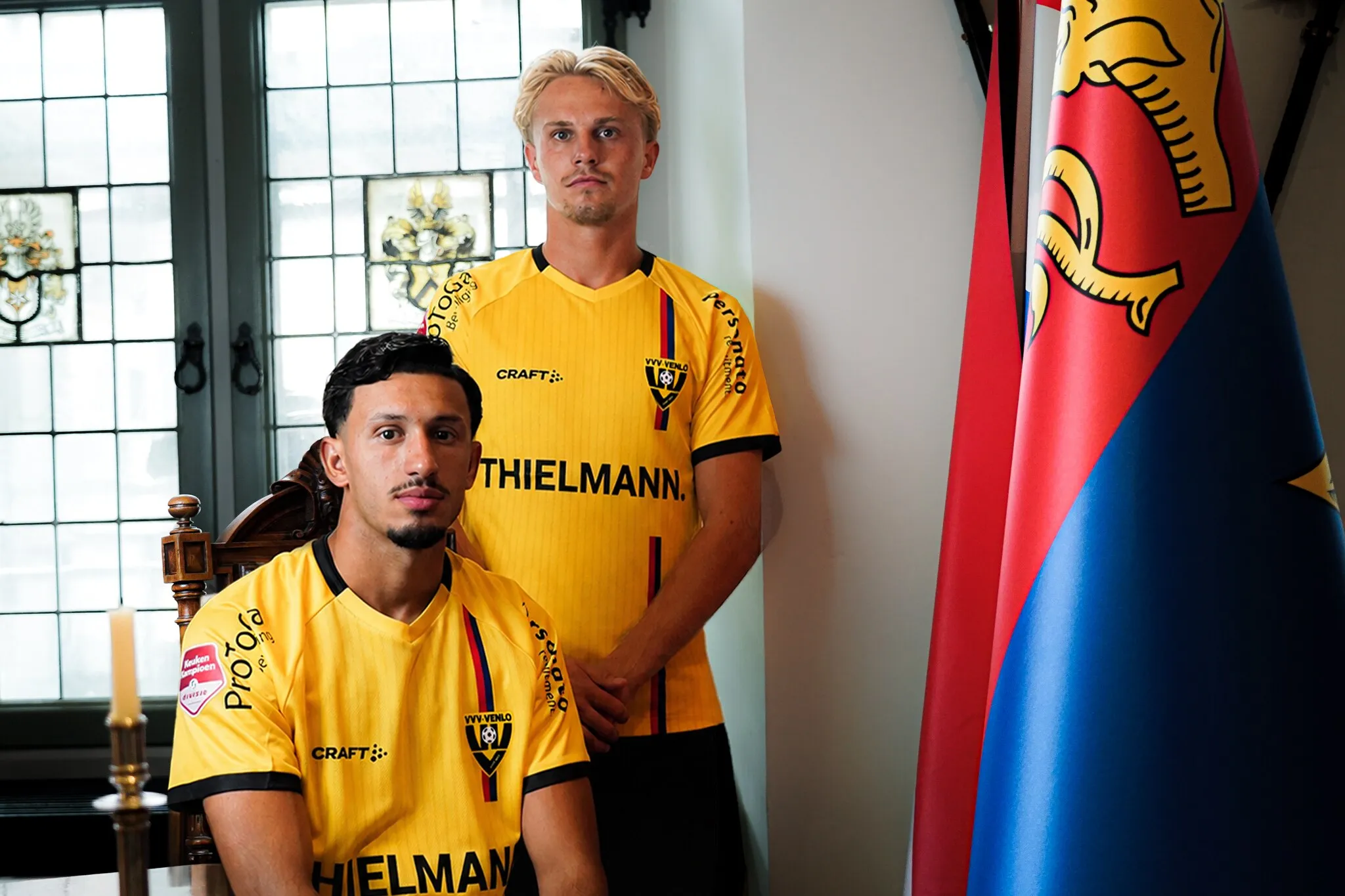 Twee spelers van VVV-Venlo poseren in een statige zaal met vlaggen